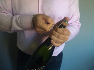 Abrir una botella de champagne o cava. Imagen. Dedo pulgar sobre el corcho, bajamos la anilla de metal y daremos seis medias vueltas hacia nosotros. Abrir una botella de champagne o cava.
